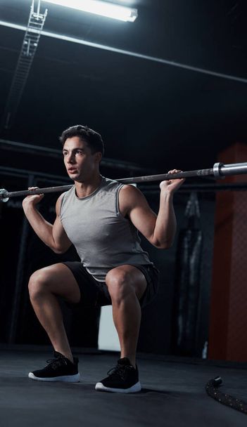 La buena salud te mantiene castigado. un joven levantando un poste de acero durante su entrenamiento en un gimnasio - Foto, Imagen