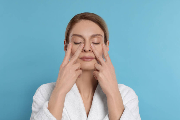 Woman massaging her face on turquoise background - Fotografie, Obrázek
