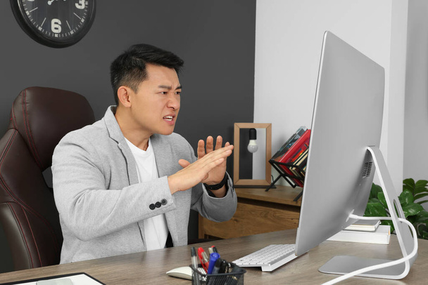 Emotional boss having online meeting via computer at wooden table in modern office - Valokuva, kuva
