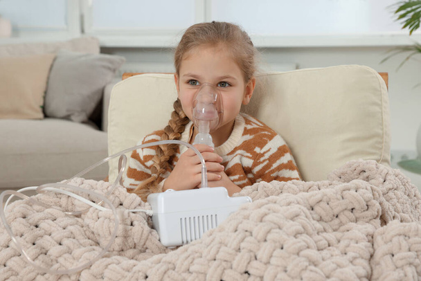 Little girl using nebulizer for inhalation in armchair at home - Фото, зображення