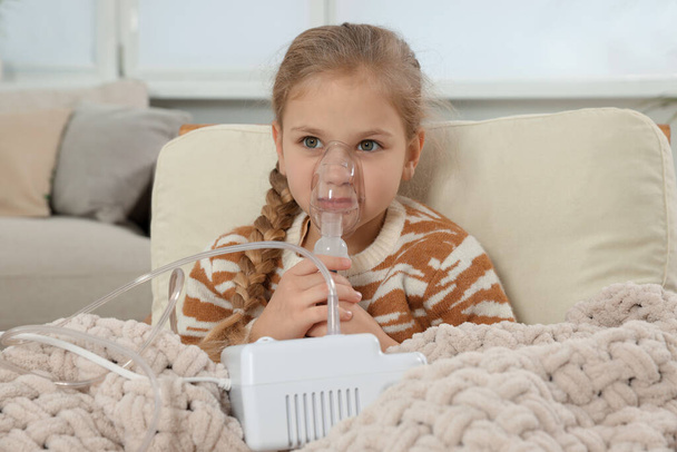 Little girl using nebulizer for inhalation in armchair at home - Foto, Imagem