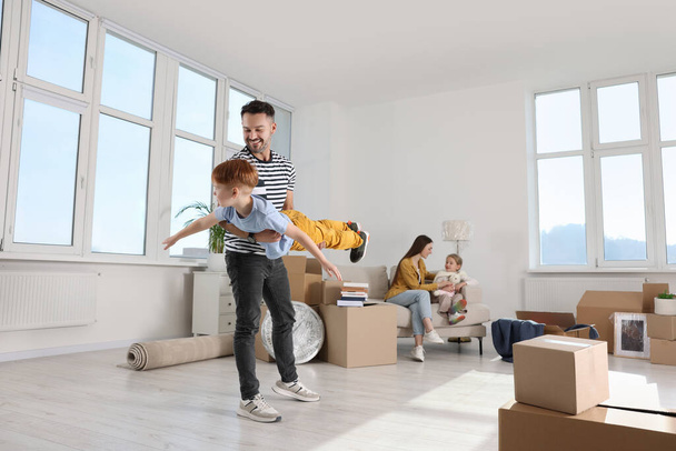Glücklicher Sohn mit Papa beim Spielen, während Mutter und Tochter auf der Couch in der neuen Wohnung sitzen. Bewegender Tag - Foto, Bild