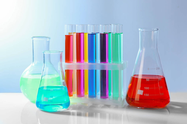 Different laboratory glassware with colorful liquids on white table against grey background - Photo, Image
