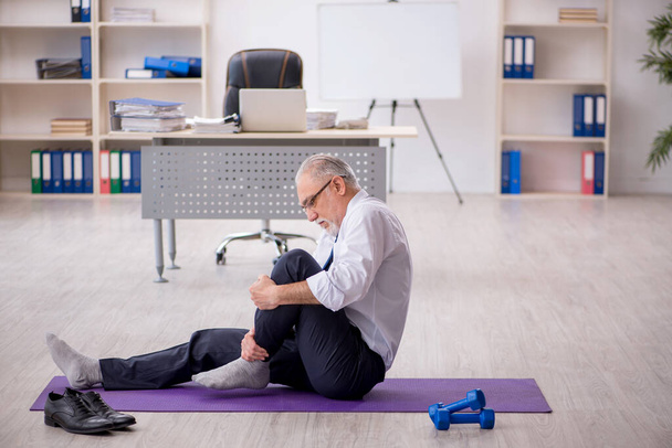 Old male employee doing sport exercises during break - Foto, afbeelding
