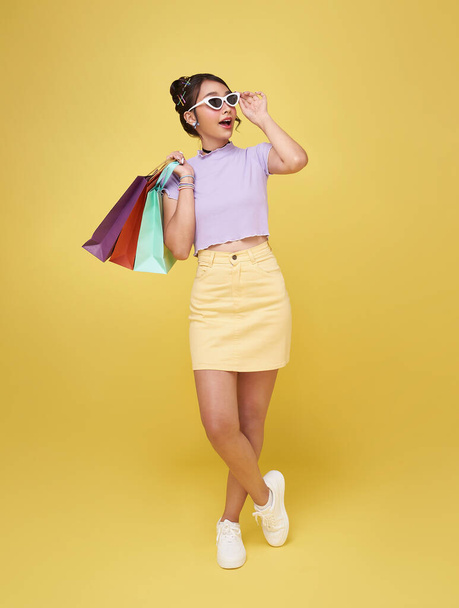 Cheerful happy thai asian woman enjoying shopping, she is carrying shopping bags isolated on  yellow background - Φωτογραφία, εικόνα