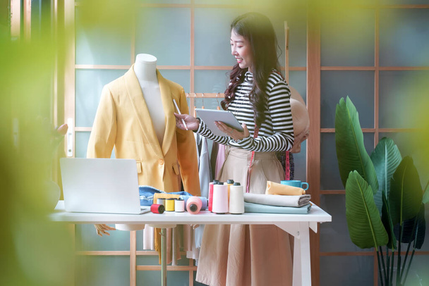 Young women fashion designer using laptop working and received order customer for design tailor and cloth in the showroom,  Lifestyle Stylish tailor taking measurements on mannequin for cutting cloths in studio.  Business SME and Industry small Conce - Photo, Image