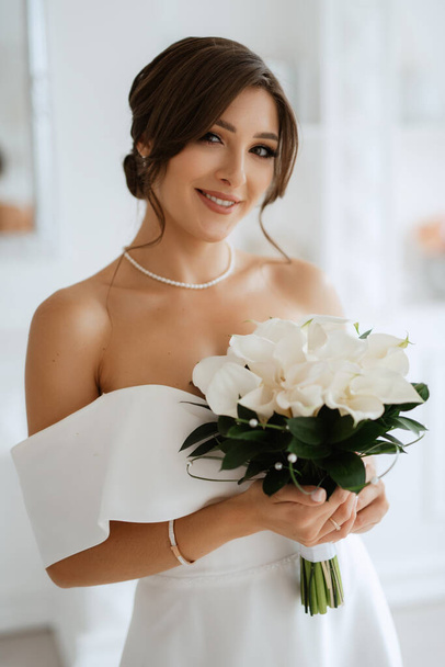 brunette bride in a tight wedding dress in a bright studio with a bouquet - Photo, image