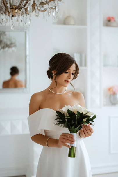 brunette bride in a tight wedding dress in a bright studio with a bouquet - Foto, imagen