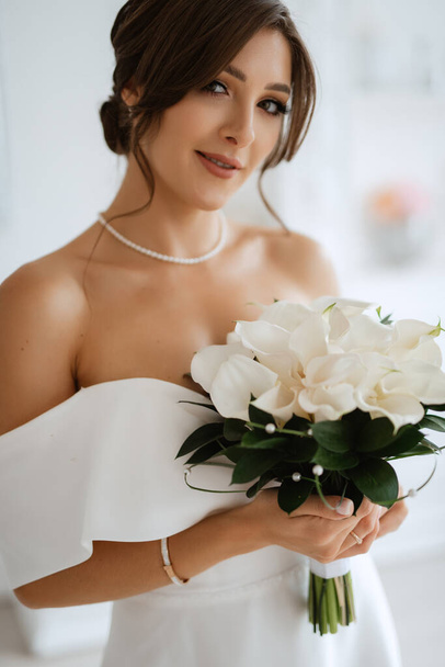 brunette bride in a tight wedding dress in a bright studio with a bouquet - Foto, afbeelding