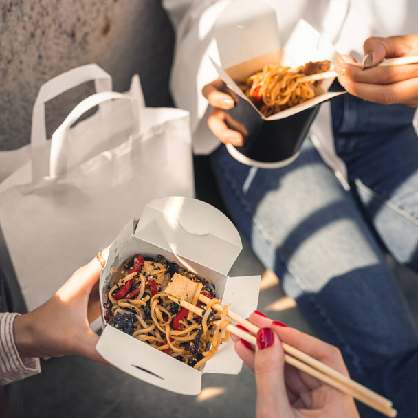 Closeup macro view of a delicious Wok Noodles with greenery in takeout paper box with chop sticks in the hands of friends - Photo, image