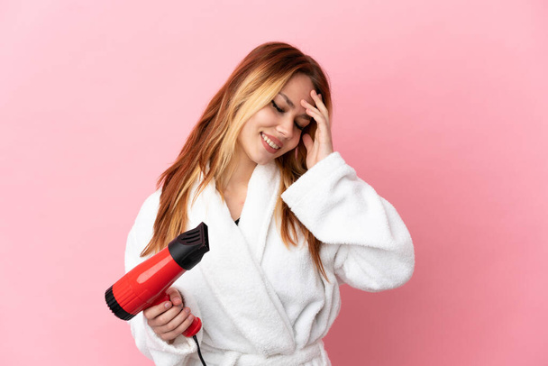 Teenager blonde Mädchen mit einem Haartrockner über isolierten rosa Hintergrund lachen - Foto, Bild