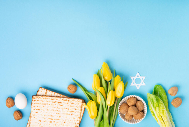 Żydowskie święto Pozdrowienia z okazji Święta Paschy koncepcja kartki z matzah matzoh (żydowski chleb wakacyjny), orzechy włoskie, żółte kwiaty tulipan na niebieskim stole. Seder Pesach wiosenne tło wakacyjne, przestrzeń do kopiowania. - Zdjęcie, obraz