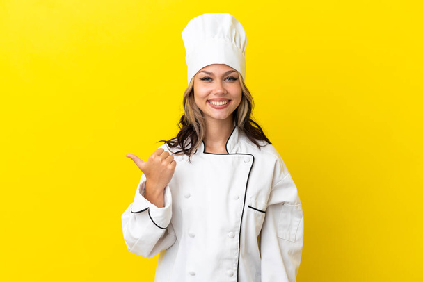 Young Russian chef girl isolated on yellow background pointing to the side to present a product - Фото, изображение