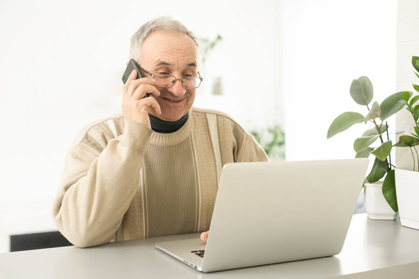 Handsome mature man in casual sitting in home office and working at laptop. - Photo, image
