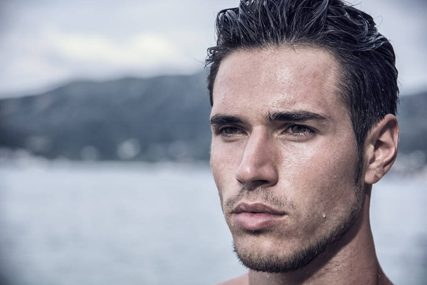 Attractive young man in the sea getting out of water with wet hair, looking away to a side - Foto, immagini