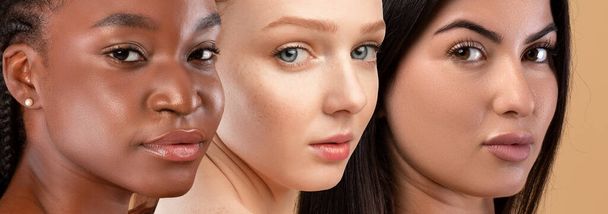 Piękne twarze młodych wielokulturowych kobiet patrzących w kamerę na beżowym tle studia, atrakcyjne panie demonstrujące idealną skórę, zbliżenie, kolaż. Piękno, pielęgnacja skóry, koncepcja pielęgnacji twarzy - Zdjęcie, obraz