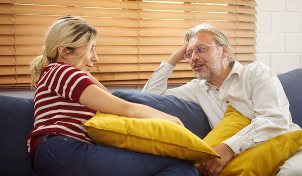 An old man and daughter talking and smiling while sitting on the sofa at home. - Fotoğraf, Görsel