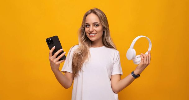meisje met een smartphone en hoofdtelefoon in haar handen op een gele achtergrond. - Foto, afbeelding