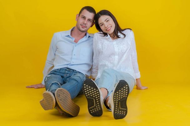 Couple smiling and sitting together on floor and looking at camera on yellow background. - Photo, Image