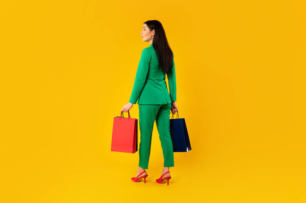 ショッピングコンセプト。黄色の背景に隔離された立って、購入を運ぶ、買い物袋を保持するスタイリッシュな女性の背面図、スタジオショット、フリーコピースペース、フル長さ - 写真・画像