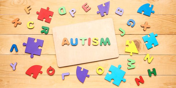Word AUTISM, letters and puzzle pieces on wooden background - Foto, afbeelding