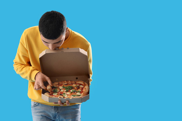 Young man with box of tasty pizza on blue background - Фото, изображение