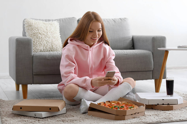 Fiatal nő ízletes pizza segítségével mobiltelefon otthon - Fotó, kép