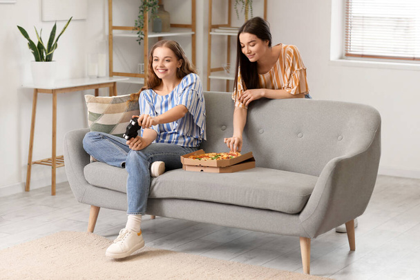 Jeunes femmes avec de savoureuses pizzas jouer à un jeu vidéo à la maison - Photo, image