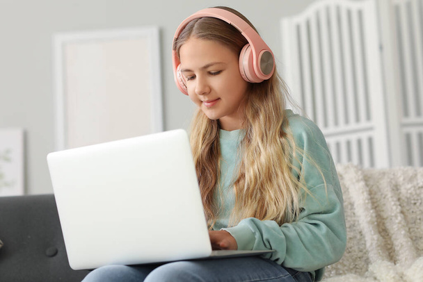 Little girl in headphones using laptop on sofa at home - 写真・画像