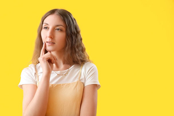 Thoughtful young woman on yellow background - 写真・画像