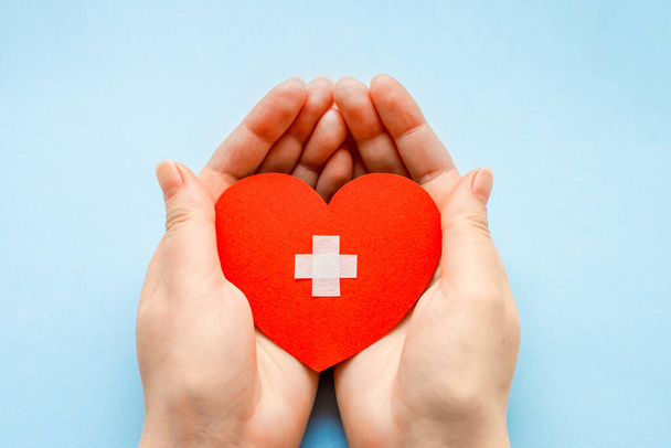 Światowy Dzień Zdrowia. koncepcja kardiologii i ludzi. zbliżenie żeńskich dłoni z krzyżykiem medycznym na małym czerwonym papierowym sercu - Zdjęcie, obraz
