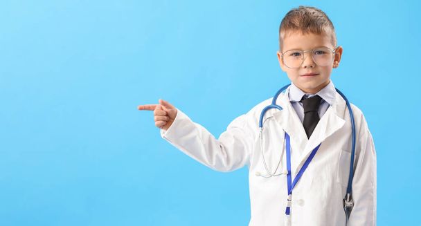 Cute little doctor pointing at something on blue background - Fotografie, Obrázek