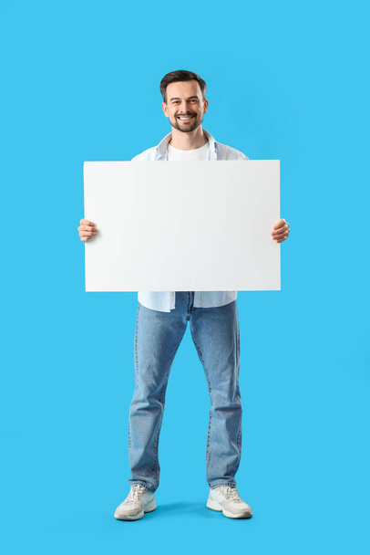 Handsome man with big blank poster on blue background - Photo, Image
