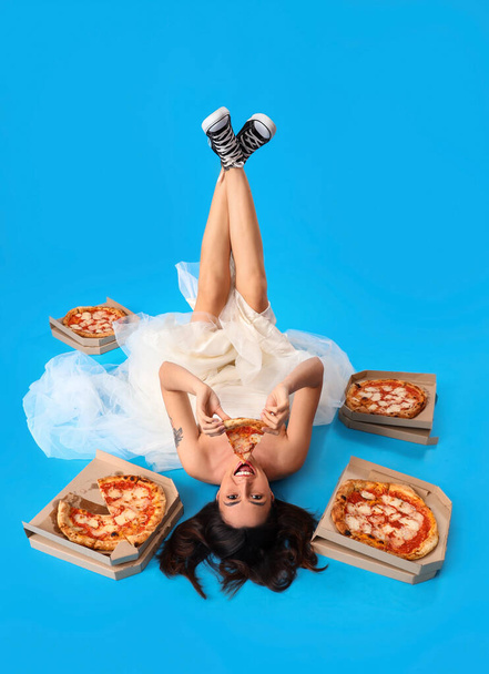 Young woman in white dress with tasty pizza lying on blue background - Фото, изображение