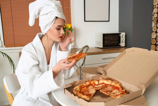 Young woman in bathrobe with tasty pizza and mirror on table at home - Photo, Image