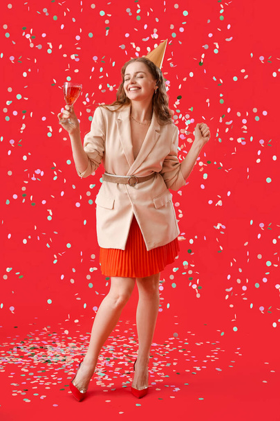 Ευτυχισμένη νεαρή γυναίκα με ποτό γιορτάζει γενέθλια σε κόκκινο φόντο - Φωτογραφία, εικόνα