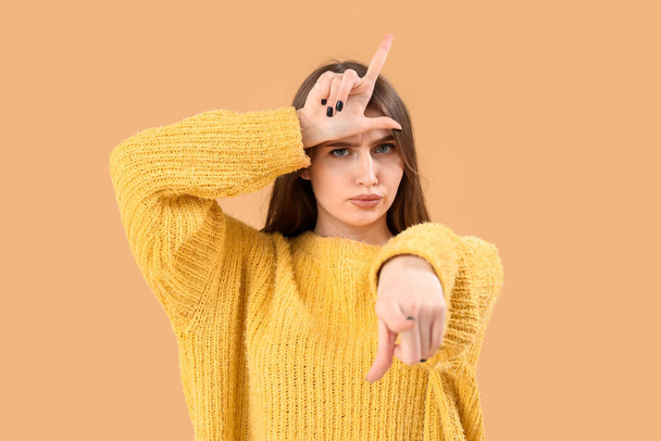 Giovane donna mostrando gesto perdente e indicando spettatore su sfondo beige - Foto, immagini