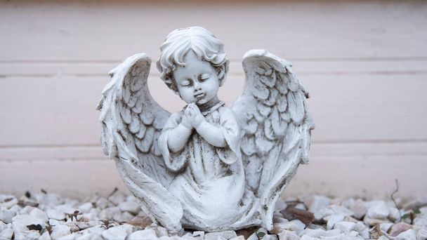 Stara, zniszczona rzeźba białego anioła. Anioł z rękami złożonymi w modlitwie i zamkniętymi oczami. - Zdjęcie, obraz