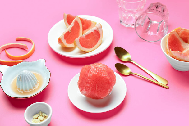Platos con pomelos maduros y exprimidor sobre fondo rosa - Foto, Imagen