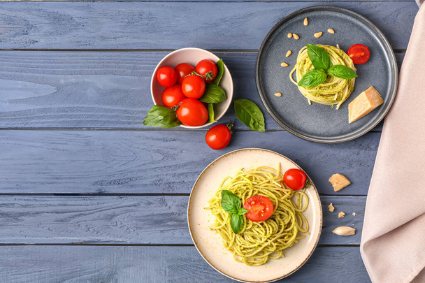 Plates with tasty pesto pasta and tomatoes on color wooden background - Fotó, kép