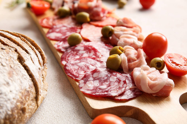 Wooden board with assortment of tasty deli meats on light background, closeup - Foto, Imagen