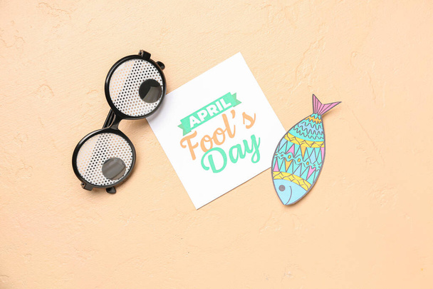 Paper with text APRIL FOOL'S DAY, fish and funny eyeglasses on beige background - Photo, Image