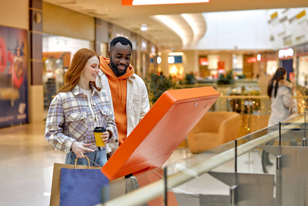 young attractive man and woman using digital navigation board to search information about shops, floors. close up side view shot - Фото, изображение