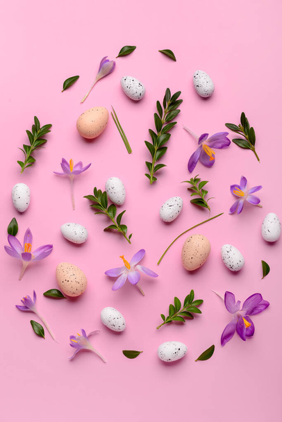 イースターエッグ、美しいクロッカスの花や植物の葉をピンクの背景に創造的な組成 - 写真・画像