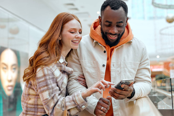 young happy girl pointing to the screen showing her bearded boyfriend sales couple choosing goods, lifestyle.hobby interests red-haired girl showing something on smart phone to handsome boyfriend - Foto, Imagem