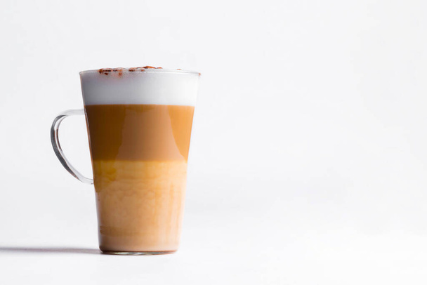 Latte macchiato in a tall glass on a white background. Cafe latte layered with milk in a high drinking glass. Minimalism. Copy space - Photo, image