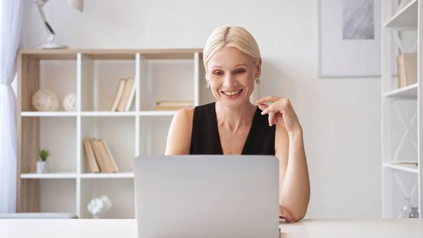 Video call. Online meeting. Remote job. Confident smiling senior business woman using notebook at light modern home office interior with free space. - Fotoğraf, Görsel