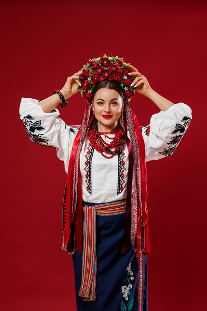 Portrait of ukrainian woman in traditional ethnic clothing and floral red wreath on viva magenta studio background. Ukrainian national embroidered dress call vyshyvanka. Pray for Ukraine - Zdjęcie, obraz