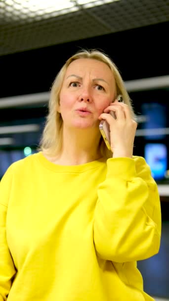 Nainen kirkkaan keltainen verkkarit puhuu vihaisesti puhelimessa hän kysyy, miksi hän ravistelee päätään tyytymättömänä yllättynyt vihainen vihainen takana toimisto tumma ikkuna yö rautatieaseman lentokentältä - Materiaali, video