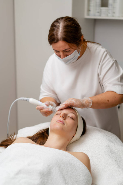 Beautician in gloves conducts vacuum cleaning and polishing face skin young woman in cosmetology clinic Professional moisturizing and rejuvenating hardware procedures for modern people - Φωτογραφία, εικόνα